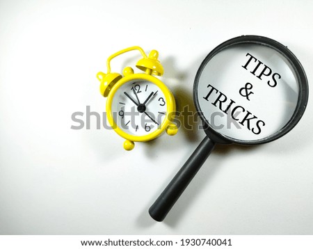 Selective focus.Word TIPS AND TRICKS with magnifying glass and clock on white background.Business concept.