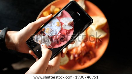 Women's hands take photos of Breakfast food using a smartphone. Fried eggs with fried potatoes, bacon and toast