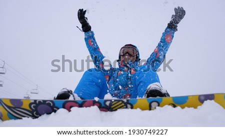 Cheerful beautiful young girl snowboarder throws snow flakes. Winter fun at the ski resort.