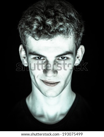 Young man with with white skin looking devilish in the dark  with a mischievous smile against a black background
