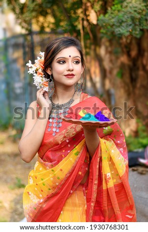 Portrait of pretty young indian girl wearing traditional saree and jewellery, holding powder colours in plate on the festival of colours called Holi, a popular hindu festival celebrated across India.  Royalty-Free Stock Photo #1930768301