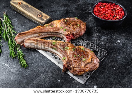 Barbecue grilled lamb chops on a butcher meat cleaver. Black background. Top view. Royalty-Free Stock Photo #1930778735