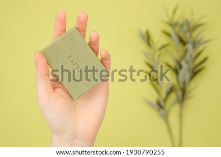 natural soap. olive branch. Hand holds a homemade soap with the inscription "olive". Sustainable hygiene products. woman holding handcrafted green soap on green surface.  homemade natural olive soap Royalty-Free Stock Photo #1930790255