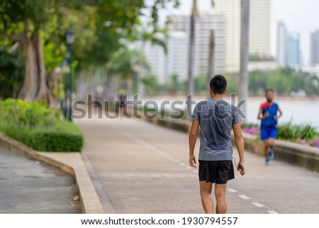 The back view of a man wearing a gray T-shirt is exercising hard, causing his back to be sweaty in the park. Royalty-Free Stock Photo #1930794557