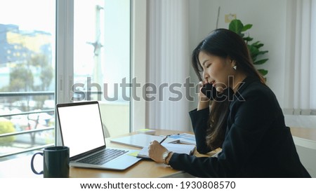 Photo a beautiful businesswoman using a smartphone to calling someone while sitting in front a computer laptop at wooden working table over comfortable living room as background.	