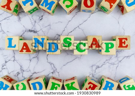 Landscape concept with colorful alphabet letters on wooden cubes centered between top and bottom borders of additional alphabet blocks on a marble background. Flat lay, top view