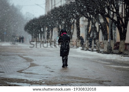 people walk through the city in a blizzard, hiding under their hoods from strong winds, cold snap and climate change