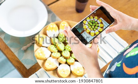 Food blogger photographs food on a smartphone. An internet influencer takes pictures of iced sugar cookies in the shape of cute chickens for Easter. Ideas for fun baking with children for Easter. 