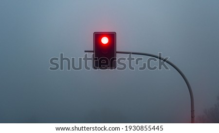 Red stop traffic light lamp during heavy fog outside the city. Mystery atmosphere. Road to nowhere.