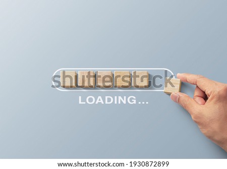 Loading, reboot, refresh or mindset concept. Hand putting wooden blocks in progress bar on gray background with the word LOADING.