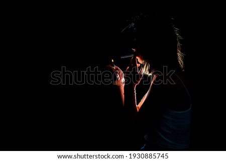 Portrait of smoking young woman on dark background. Cigarette concept. Blue smoke. Horizontal shot.