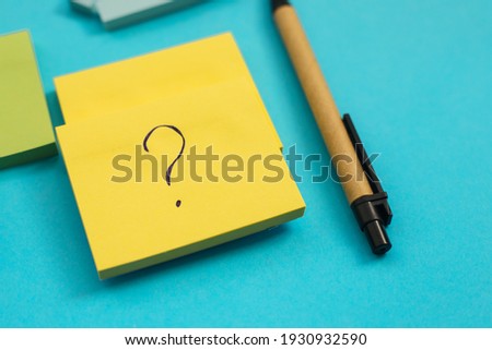 Stickers of different sizes and colors are placed on a blue background. There's a pen next to it. Notepads for notes and reminders. A question mark is written on the leaf.