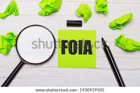 The words FOIA The Freedom of Information Act written on a green sticky note next to a magnifying glass and a black marker on a wooden table
