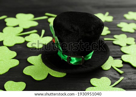 Leprechaun's hat and decorative clover leaves on black wooden background. St. Patrick's day celebration