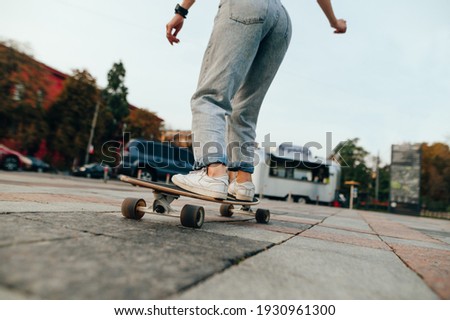 Back view, cropped shot of a female skateboarder riding long board on a concrete pavement. City street on a background.