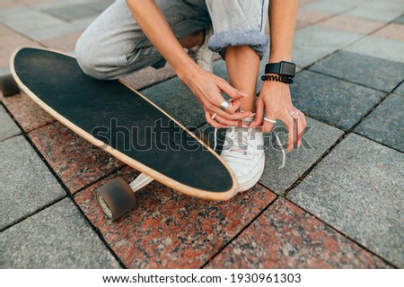 Closeup photo of a female's hands tying her shoelaces. Woman with a skateboard is tying her sneakers on a concrete pavement.