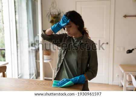 I feel for you poor Cinderella. Exhausted millennial housewife in blue latex gloves wipe sweat from brow. Sad fatigued young woman too tired of household chores cleaning flat house dusting furniture Royalty-Free Stock Photo #1930961597