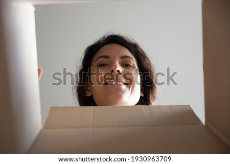 Curious smiling millennial female face look inside postal parcel open unpack delivery get present surprise by mail. Happy young woman customer receive purchase from web shop packed in cardboard box Royalty-Free Stock Photo #1930963709