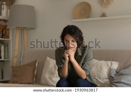 Critical situation. Thoughtful nervous young lady sit on sofa lean forward on folded hands try to keep emotions under control. Worried female think of overcoming bad life event ponder on hard decision Royalty-Free Stock Photo #1930963817