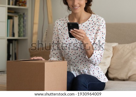 Cropped shot of young lady shopper sit on sofa hold delivered package with consumer goods text good feedback to online shop website. Smiling female video blogger shoot unpacking process on cell webcam