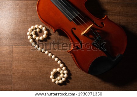 Violin and pearl necklace, arrangement with violin and pearl necklace on wooden surface, low key portrait, Top view.