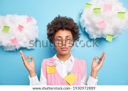 Calm relaxing female office worker feels relieved and stress free meditates indoor keeps eyes closed surrounded with colorful sticky notes takes break from work for mental balance avoids stressful job