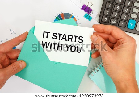 The businessman takes out a card from the envelope with the text IT STARTS WITH YOU, on the background of the office desk.