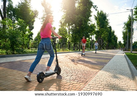 Three young girl friends on the electro scooters having fun in city street at summer sunny day. Outdoor portrait of three friends girl riding electric kick scooter in the park.