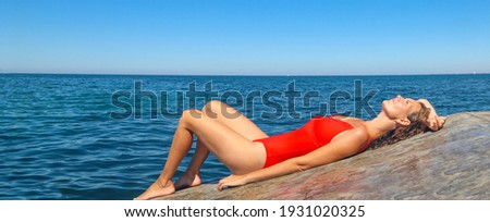 beautiful girl in a red swimsuit sunbathes on a concrete pier against the background of the blue sea