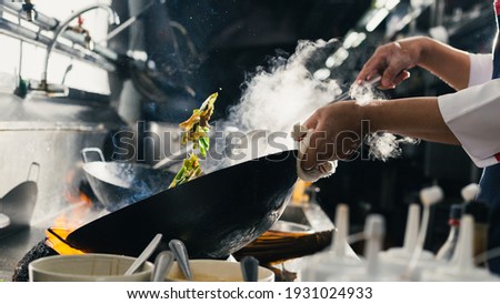 Chef stir fry busy cooking in kitchen. Chef stir fry the food in a frying pan, smoke and splatter the sauce in the kitchen. Royalty-Free Stock Photo #1931024933