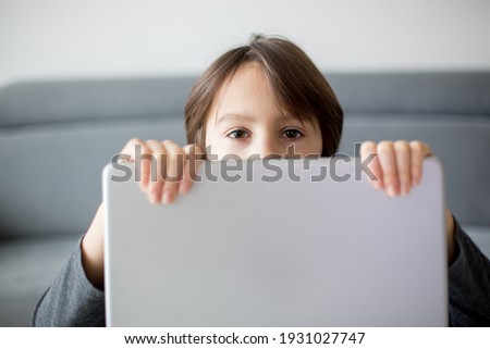Preteen child, hiding behind notebook, online education, games and fun for kid, computer as bad influence for children
