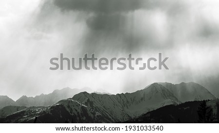 sunbeams and dark clouds over the snow capped alps in austria in black and white photography