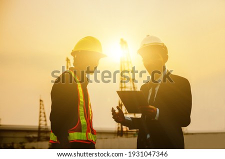 Construction engineers use tablet communications against building construction site backgrounds in the morning.