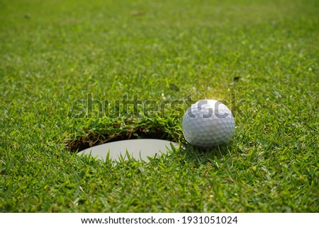 Golf ball and golf hole on green grass. A golf ball sits at the lip of the hole on the putting green. white golf ball near hole on fairway with the green background in the country side.