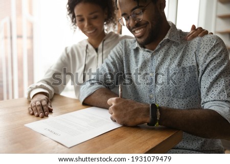 Close up smiling African American family signing contract, making successful investment or insurance deal, happy man husband wearing glasses putting signature, filling document, taking loan