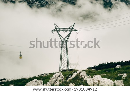 A cable car passing through the clouds on the tops of the Alpine Mountains, where a lone yellow cab seems to float in the sky.