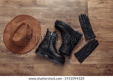 Women's accessories. Black Leather boots, gloves and hat on wooden floor. Top view. Flat lay