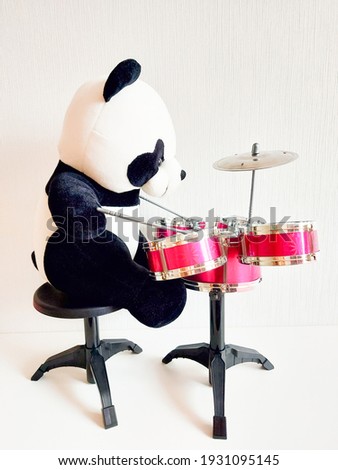 Panda plays the drum. Black and white stuffed panda bear. Toy is reddy. Talented bear.