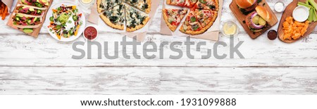 Healthy plant based fast food top border. Above view over a white wood banner background. Table scene with cauliflower crust pizzas, bean burgers, mushroom tacos and vegetarian sides. Copy space.