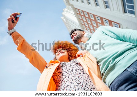 Young couple taking a photo with mobile phone with buildings in the background - Technology concept