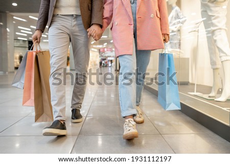 Close-p of young couple holding hands and walking together in shopping mall with purchases Royalty-Free Stock Photo #1931112197