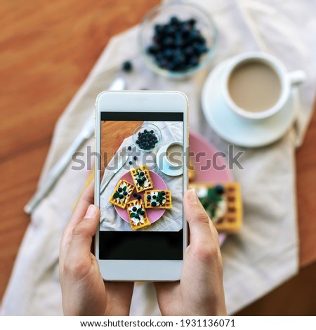Girl's hands taking pictures of healthy waffles with blueberries by phone, top view.