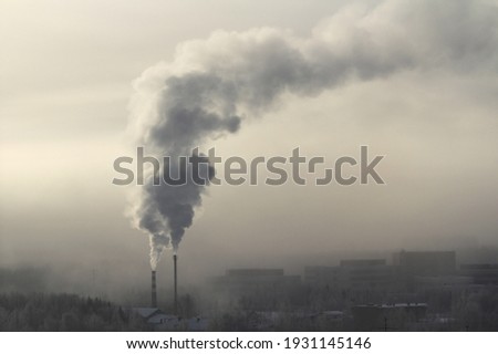 Sun below the horizon and clouds, light gray sky at sunset or dawn backlit by the sun. City panorama in a foggy haze, smoke from a chimney. Place for text and design. Royalty-Free Stock Photo #1931145146