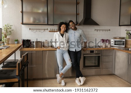 Full length portrait happy African American couple standing in modern kitchen at home, smiling wife and husband excited by relocation, satisfied clients purchased new apartment, mortgage concept Royalty-Free Stock Photo #1931162372