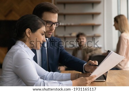 Close up diverse colleagues working together, checking documents, reading report, Indian businesswoman and Caucasian businessman discussing project statistics, mentor coach training intern in office Royalty-Free Stock Photo #1931165117