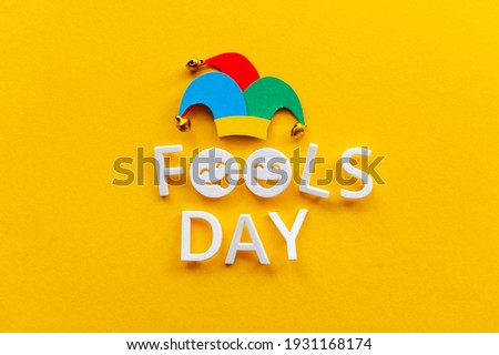 April fools day over yellow background with jester hat. First April card with happy face emojis. Copy space for text, top view.  