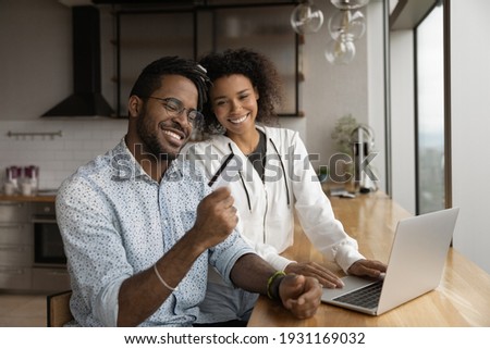 Close up happy African American couple paying online by credit card, using laptop, smiling wife and husband shopping, purchasing, browsing banking service, making internet secure payment at home