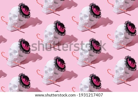 White skull with glamour hat on pink pastel background eats candy cane. Christmas minimal mood concept. New Year’s greeting card. Pattern with skull. Halloween inspiration.