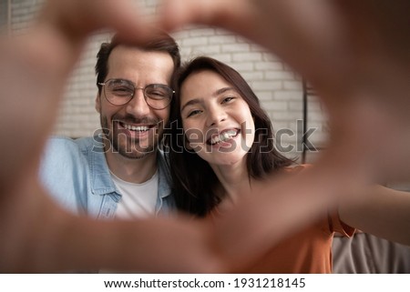 Happy Valentine day. Selfie portrait of romantic family couple holding heart of joined fingers looking at camera. Happy young spouses feel thankful grateful to destiny for meeting love strong marriage Royalty-Free Stock Photo #1931218145