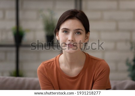 Headshot portrait of confident millennial woman sit on sofa at living room looking at camera webcam take part in virtual event conference. Young female student having online job interview by videocall